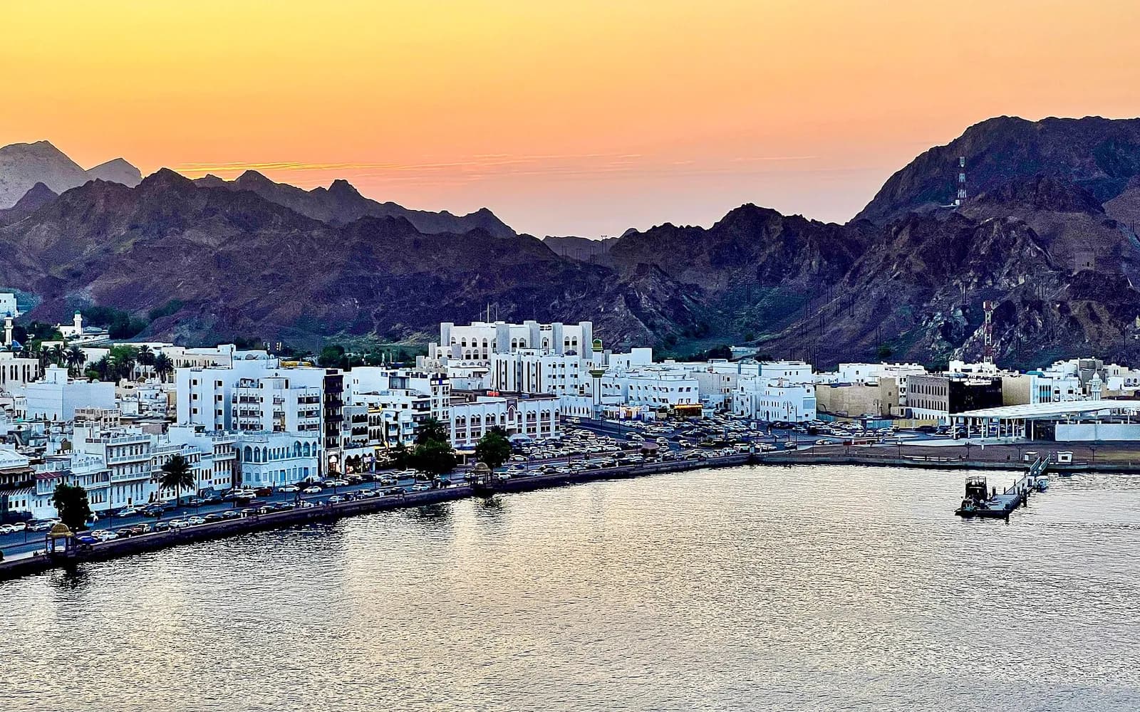 غروب فوق الجبال مع المباني السكنية والسوق على واجهة مطرح البحرية